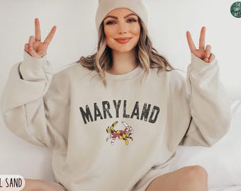 May include: Sand-colored sweatshirt with the word "MARYLAND" in distressed black lettering and a crab graphic. The Simple West logo is in the upper right corner. The sweatshirt is XL size.