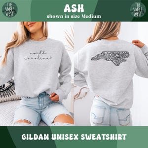 May include: Ash-colored Gildan unisex sweatshirt. The front features the script "north carolina". The back displays a detailed black design of the North Carolina state outline. The Simple West logo is visible. The sweatshirt is shown in size Medium.