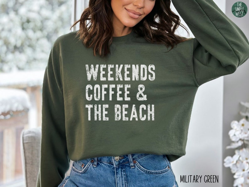 May include: A green sweatshirt with the text "Weekends Coffee & The Beach" in white distressed lettering. The sweatshirt is shown on a model wearing blue jeans.