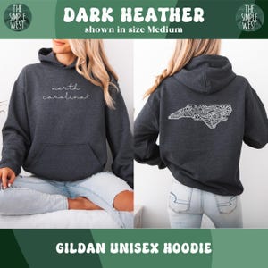 May include: Dark heather gray Gildan unisex hoodie. The front features the text "north carolina" in a cursive font. The back displays a white, detailed outline of North Carolina. The Simple West logo is visible.