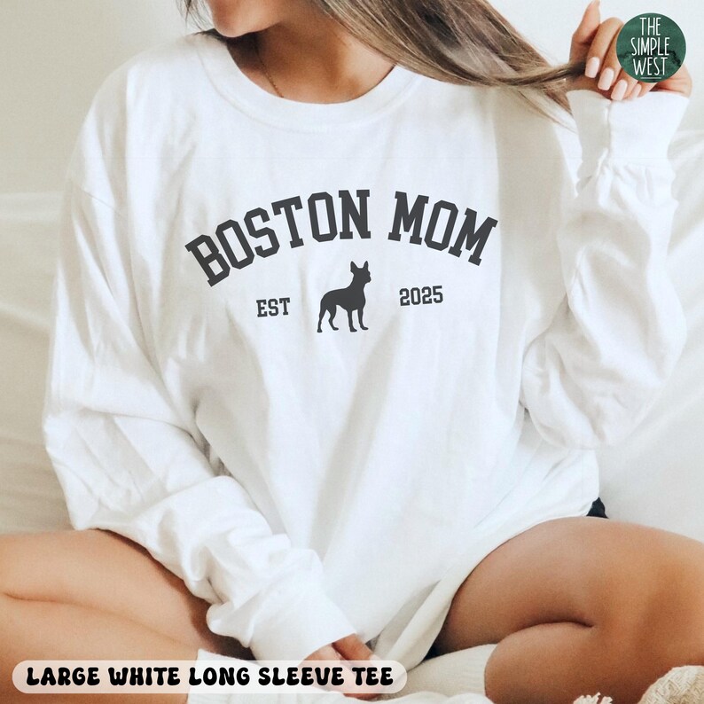 Puede incluir: Camiseta blanca de manga larga con el texto "BOSTON MOM" en gris oscuro, una silueta de perro y el a&ntilde;o "2025". La camiseta tambi&eacute;n tiene el texto "LARGE WHITE LONG SLEEVE TEE" en la parte inferior.
