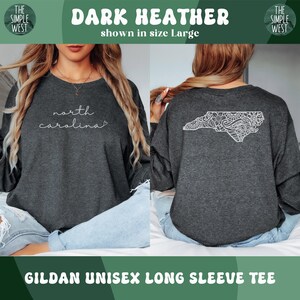 May include: Dark heather long-sleeve tee with "north carolina" in white script on the front. The back features a white, detailed outline of North Carolina. The shirt is a Gildan unisex long sleeve tee.