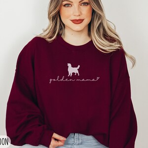 May include: A maroon sweatshirt with a pink silhouette of a golden retriever and the text "golden mama" in pink script.