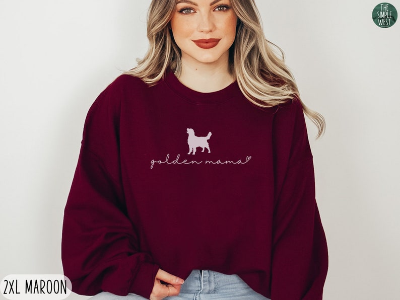 May include: A maroon sweatshirt with a pink silhouette of a golden retriever and the text "golden mama" in pink script.