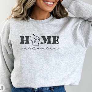 May include: Gray sweatshirt with the text "HOME wisconsin" in black. The word "HOME" has a stylized outline and a heart inside the letter "O". The state of Wisconsin is depicted inside the letter "O".