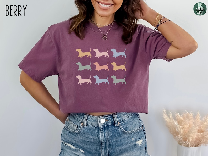 May include: A purple cropped t-shirt featuring a graphic of nine pastel coloured dachshund silhouettes. The text "BERRY" is in the top left corner of the image.