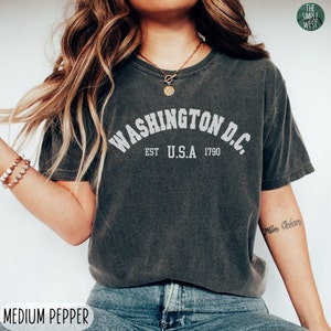 May include: A dark gray t-shirt with a white graphic that says "WASHINGTON D.C. EST U.S.A. 1790".