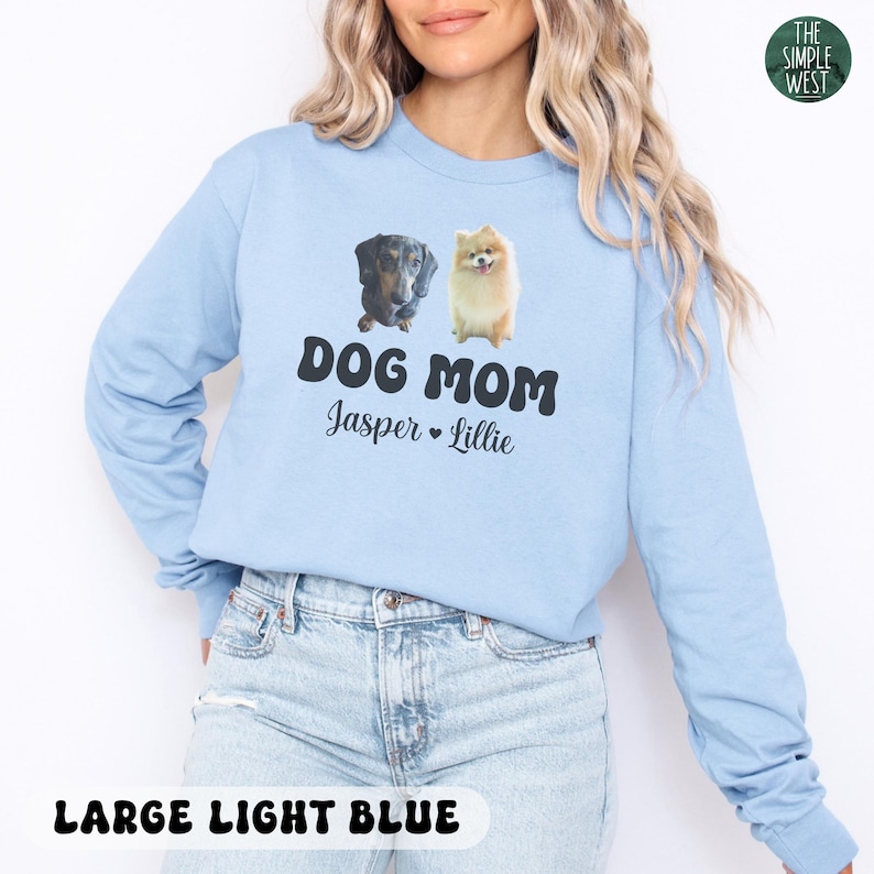 May include: Light blue long-sleeve shirt with the text "DOG MOM" and the names "Jasper" and "Lillie" printed in black. The shirt features images of a dachshund and a Pomeranian. The words "LARGE LIGHT BLUE" are printed at the bottom.