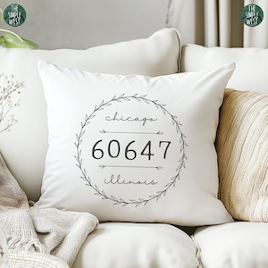 May include: White throw pillow with a black and white design featuring a wreath with the words "chicago 60647 illinois" inside.