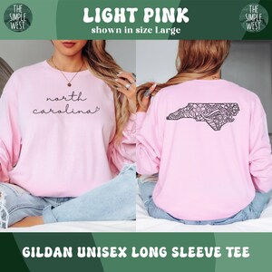 May include: Light pink Gildan unisex long sleeve tee. The front features the text "north carolina" in a script font. The back displays a black graphic of the North Carolina state outline with a decorative pattern. The shirt is shown in size Large.