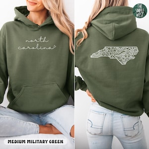 May include: Medium military green hoodie with the words "north carolina" in cursive on the front. The back features a white, detailed outline of the North Carolina state shape. The Simple West logo is in the top right corner.
