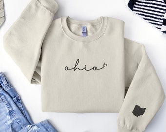 May include: A light beige sweatshirt with the word "ohio" written in black cursive with a small heart next to it. The sweatshirt has a black outline of the state of Ohio on the left sleeve.