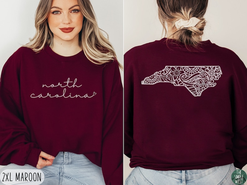 May include: Maroon sweatshirt with the text "north carolina" in white script on the front and a white outline of the state of North Carolina with a floral design on the back.