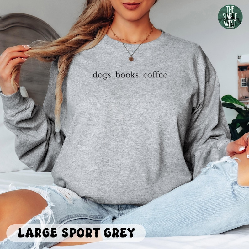 May include: A light gray sweatshirt with the text "dogs. books. coffee" in a simple font. The sweatshirt is labeled "LARGE SPORT GREY" at the bottom. The Simple West logo is in the upper right corner.