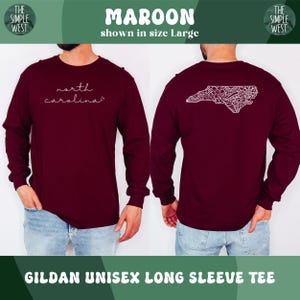 May include: Maroon Gildan unisex long sleeve tee. The front of the shirt has the words "north carolina" in a cursive font. The back of the shirt has a white design of the North Carolina state outline.