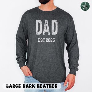 May include: Dark heather gray long-sleeve shirt with the word "DAD" in distressed white lettering above "EST 2025". The shirt is a large size and is made of a soft, comfortable material. The Simple West logo is in the upper right corner.
