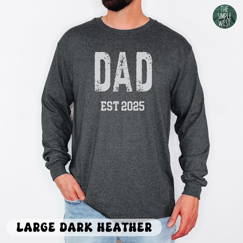 May include: Dark heather gray long-sleeve shirt with the word "DAD" in distressed white lettering above "EST 2025". The shirt is a large size and is made of a soft, comfortable material. The Simple West logo is in the upper right corner.