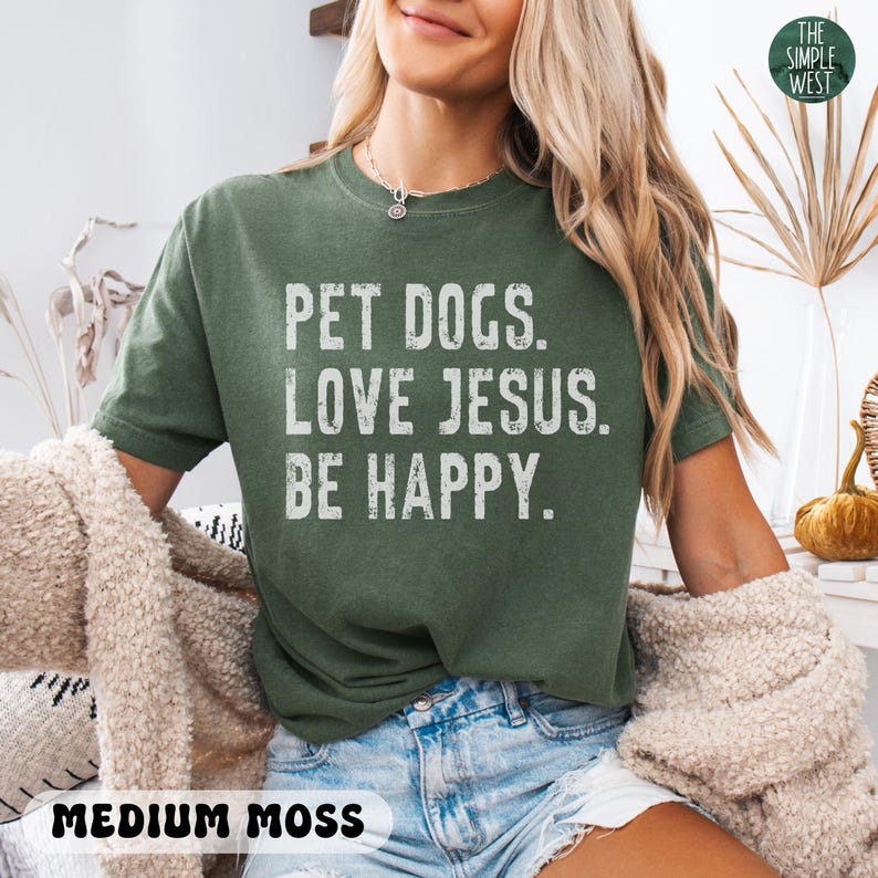 Puede incluir: Camiseta verde musgo medio con el texto "PET DOGS. LOVE JESUS. BE HAPPY." en blanco. La camiseta es de corte holgado y tiene mangas cortas. Las palabras "MEDIUM MOSS" est&aacute;n impresas en negro en la parte inferior de la camiseta.