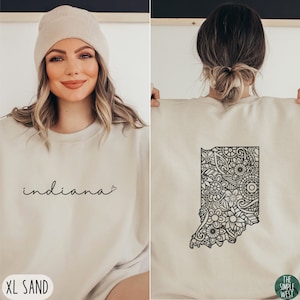 May include: A sand-colored sweatshirt with the word "indiana" and a heart on the front. The back of the sweatshirt features a black and white mandala design of the state of Indiana.
