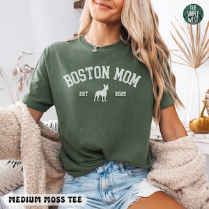 Puede incluir: Una camiseta verde musgo medio con el texto blanco "BOSTON MOM", una silueta de perro y "EST 2025". La camiseta tambi&eacute;n tiene el texto "MEDIUM MOSS TEE" en la parte inferior.