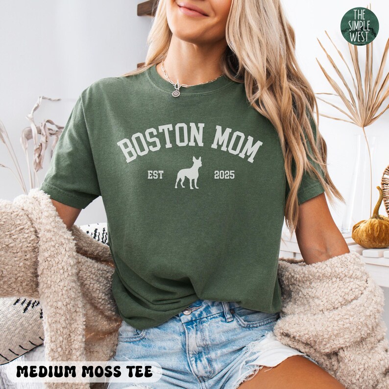 Puede incluir: Una camiseta verde musgo medio con el texto blanco "BOSTON MOM", una silueta de perro y "EST 2025". La camiseta tambi&eacute;n tiene el texto "MEDIUM MOSS TEE" en la parte inferior.