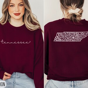 May include: A maroon sweatshirt with the word "Tennessee" in white script on the front and a white outline of the state of Tennessee with a floral design on the back.