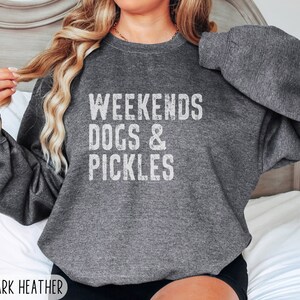 Op de afbeelding: Een donker grijs sweatshirt met de tekst "Weekends Dogs & Pickles" in wit.