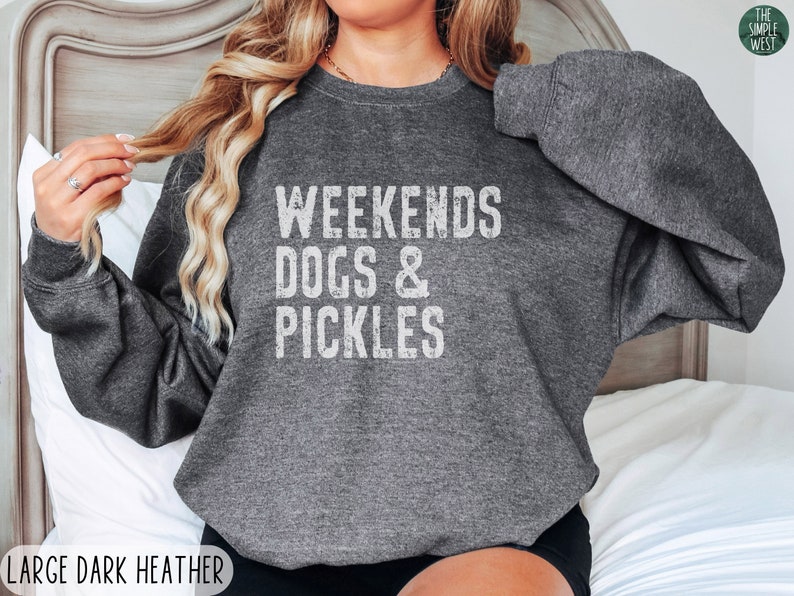 Op de afbeelding: Een donker grijs sweatshirt met de tekst "Weekends Dogs & Pickles" in wit.
