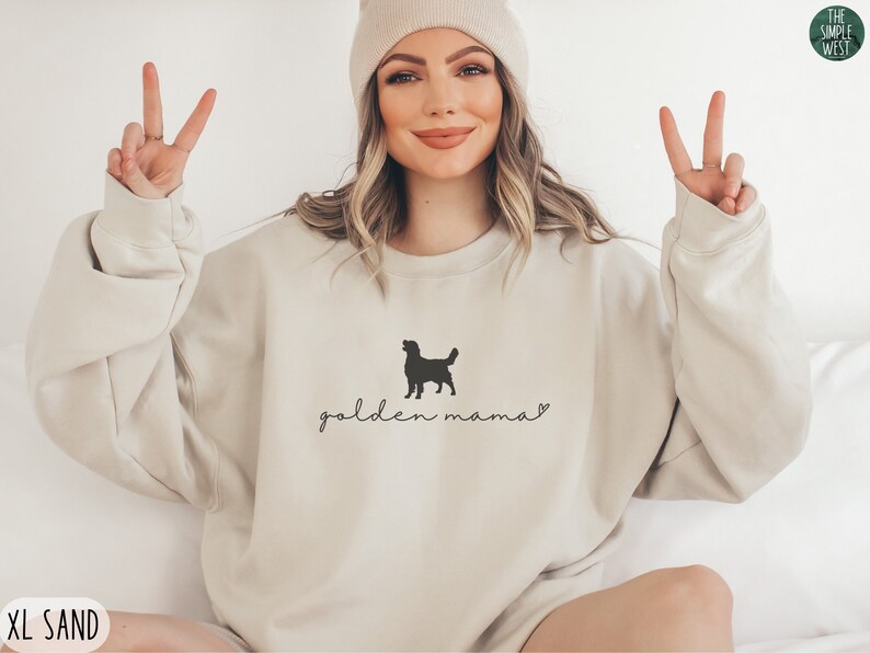 May include: A beige sweatshirt with a black silhouette of a golden retriever and the text "golden mama" in black cursive.