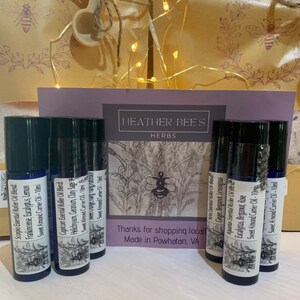 May include: A set of ten 10 ml essential oil roller bottles with labels featuring zodiac signs and corresponding essential oil blends. The labels also include the text "HEATHER BEE'S HERBS" and "Thanks for shopping local. Made in Powhatan, VA".