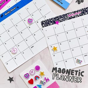Puede incluir: Planificadores mensuales blancos con bordes coloridos e imanes decorativos. Los planificadores tienen un diseño de cuadrícula con fechas y el texto "Monthly Planner". La imagen también incluye un paquete de imanes "Monthly Organizer Pin".