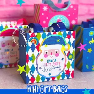 Puede incluir: Mini bolsas de regalo con gráficos de Papá Noel y el texto "Have a Holly Jolly Christmas". Las bolsas presentan un patrón de diamantes en azul, verde y blanco, con asas de cinta azul. Se ven bolsas adicionales en rosa y azul, con detalles de estrellas.