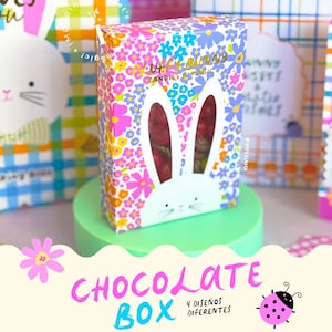 Puede incluir: Una caja de bombones colorida con un estampado floral y un diseño de conejito. La caja tiene un recorte de orejas de conejo, que revela el contenido. El texto "CHOCOLATE BOX" se muestra en rosa y azul, con "4 DISEÑOS DIFERENTES" debajo.