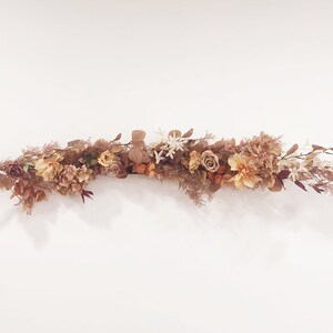 May include: A garland of dried flowers in shades of brown, beige, and white. The garland is made of various types of flowers, including roses, hydrangeas, and sprigs of greenery.