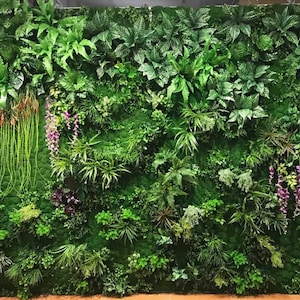 May include: A green artificial plant wall with a variety of textures and colors. The wall is made up of different types of plants, including ferns, vines, and moss. The wall is perfect for adding a touch of nature to any room.