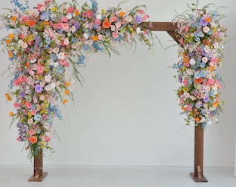 May include: A wooden wedding arch adorned with a vibrant array of colorful flowers. The floral arrangement includes pink, orange, blue, purple, and white blooms, creating a cheerful and romantic atmosphere. The arch is a beautiful backdrop for ceremonies.