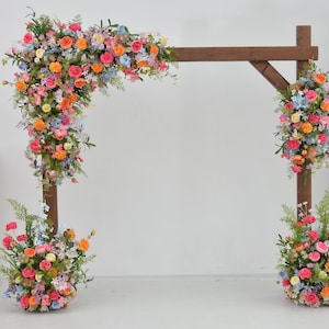 Composizione floreale Arch Wildflowers con rosa acceso, azzurro, arancione e viola pallido