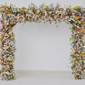 Composizioni floreali per matrimoni con pergolato di fiori selvatici in una tavolozza pastello con un tocco di arancione e azzurro