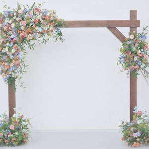 Composizioni floreali per matrimoni con pergolato di fiori selvatici in una tavolozza pastello con un tocco di viola e azzurro