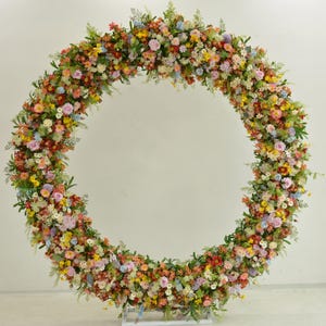 May include: A large circular floral arrangement made of a variety of colorful flowers, including pink, yellow, orange, and purple. The flowers are arranged in a circle around a metal frame, creating a beautiful and festive backdrop.