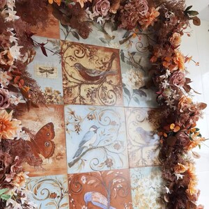 May include: A decorative tile design featuring a patchwork of colorful tiles with floral and bird motifs. The tiles are surrounded by a garland of dried flowers in shades of brown, pink, and white.