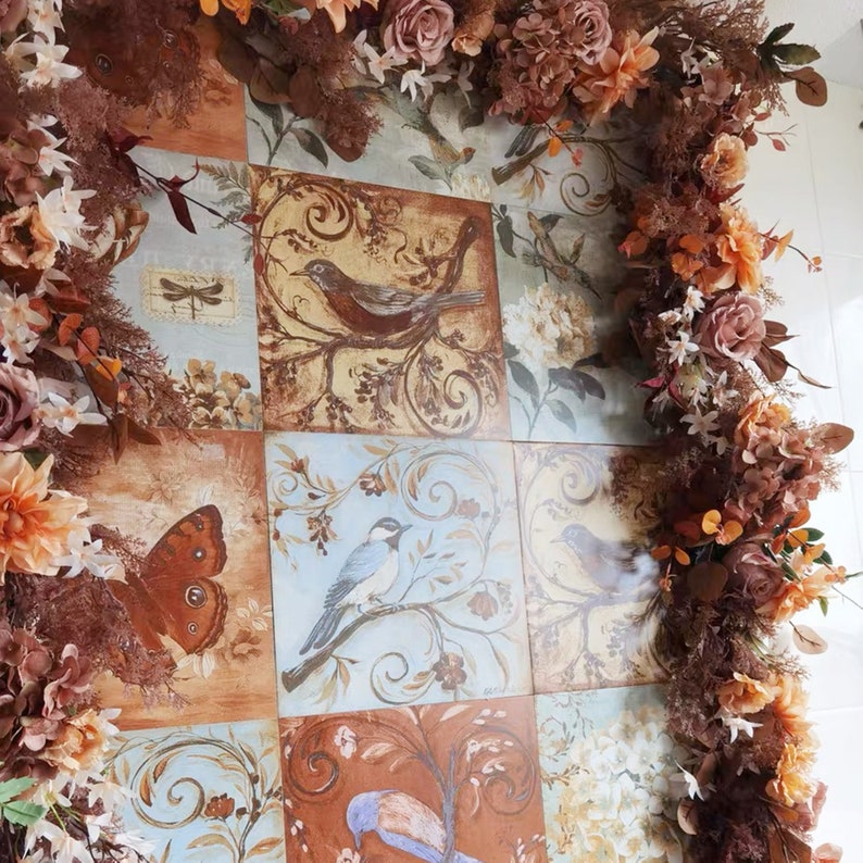 May include: A decorative tile design featuring a patchwork of colorful tiles with floral and bird motifs. The tiles are surrounded by a garland of dried flowers in shades of brown, pink, and white.