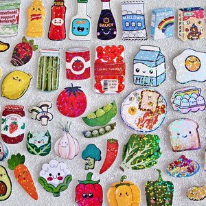 May include: A collection of colorful food-themed stickers, including fruits, vegetables, condiments, and breakfast items. The stickers feature cute, cartoon-like designs with glitter accents. Items include a banana, tomato, milk carton, and popcorn.