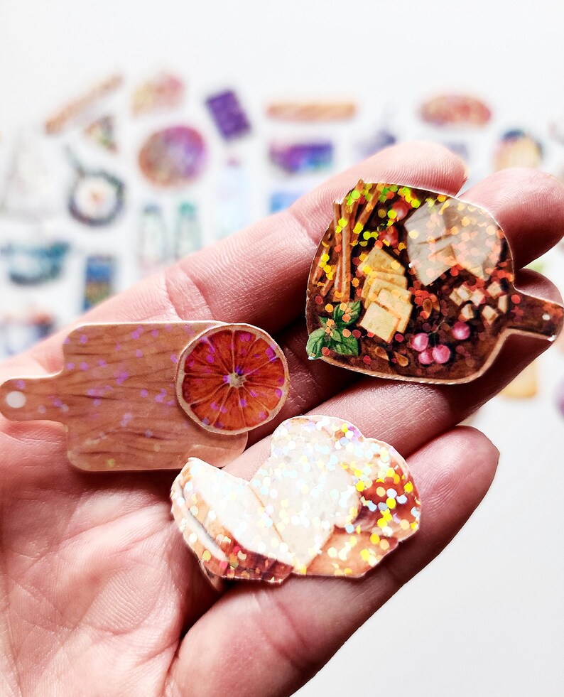 May include: Three holographic stickers featuring a cutting board with a slice of orange, a loaf of bread, and a charcuterie board with cheese, grapes, and crackers.