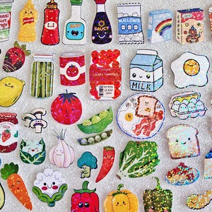 May include: A collection of colorful, illustrated food stickers, including fruits, vegetables, condiments, and breakfast items. The stickers feature smiling faces and playful designs, such as a banana, watermelon, and a carton of milk. The text "emotional support beverage" is visible on a cup.