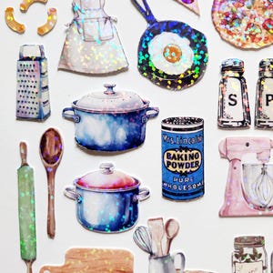 May include: A set of iridescent holographic stickers featuring kitchen items like a rolling pin, wooden spoon, grater, a pot, a pan, a cutting board, a whisk, a spatula, a mixing bowl, a jar of oregano, a can of baking powder, a stand mixer, and a pizza.