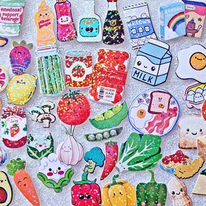 May include: A collection of colorful food-themed stickers, including a banana, milk carton, egg, tomato, and various fruits and vegetables. The stickers have a cartoon style with smiling faces and bright colors. The stickers are arranged on a white surface.
