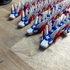 May include: A collection of red, white, and blue dragon-shaped ornaments. The dragons have white spikes, red wings, and blue heads with white stars. The ornaments are arranged on a wooden surface.