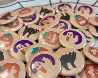 May include: A collection of Halloween themed button pins featuring various designs including ghosts, pumpkins, and black cats. The pins are round and have a beige background with colorful illustrations.