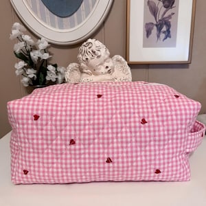 Può includere: Trucco rosa trapuntato con motivo a quadri bianchi e cuori rossi ricamati.